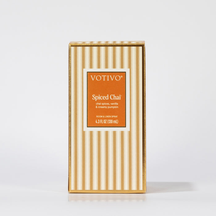 A rectangular box of Votivo Spiced Chai Room & Linen Spray features beige and white vertical stripes with an orange front label displaying the fabric-safe product name and scent details.