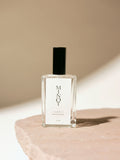 Clear glass bottle of MINOT Summit room and linen spray with black cap, placed on a textured stone surface, highlighted by soft natural light.