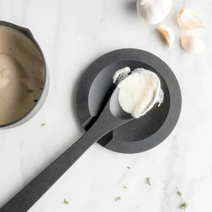 Top-down view of Slate Round tool rest showcasing a black serving spoon with garlic cream on a white marble background