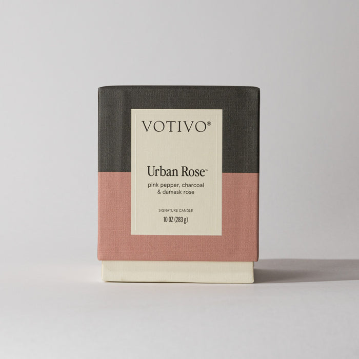 The Votivo Urban Rose 10 oz. Signature Candle features a color-block black, pink, and cream box and a label highlighting its pink pepper, charcoal, and damask rose scent with soy blend wax (283 g) inside.