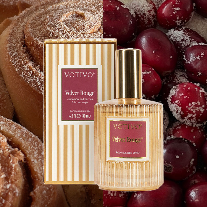 A Votivo Velvet Rouge Room & Linen Spray bottle and box are set among cinnamon rolls and red berries, capturing a cozy, festive atmosphere.