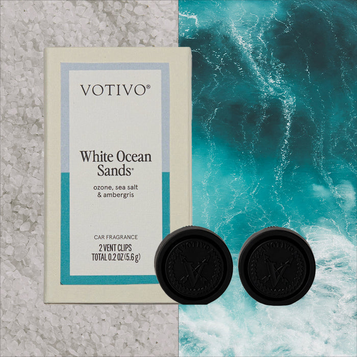 A Votivo White Ocean Sands Car Fragrance (2 Pack) and two black vent clips are shown on a background of white sea salt to the left and turquoise ocean to the right.