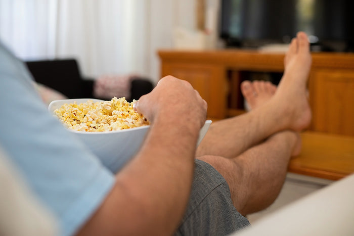 Person holding a bowl of popcorn with legs stretched out, relaxing indoors.