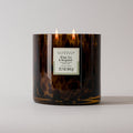 A brown, speckled tortoise jar holds a lit Votivo White Tea & Bergamot Tortoise Candle (22.7 oz), made from soy blend wax with two flames and a white front label displaying the weight.