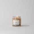 A Votivo Wilde Discovery Candle burns softly in a clear glass jar, filling the air with lasting fragrance against a plain white background.