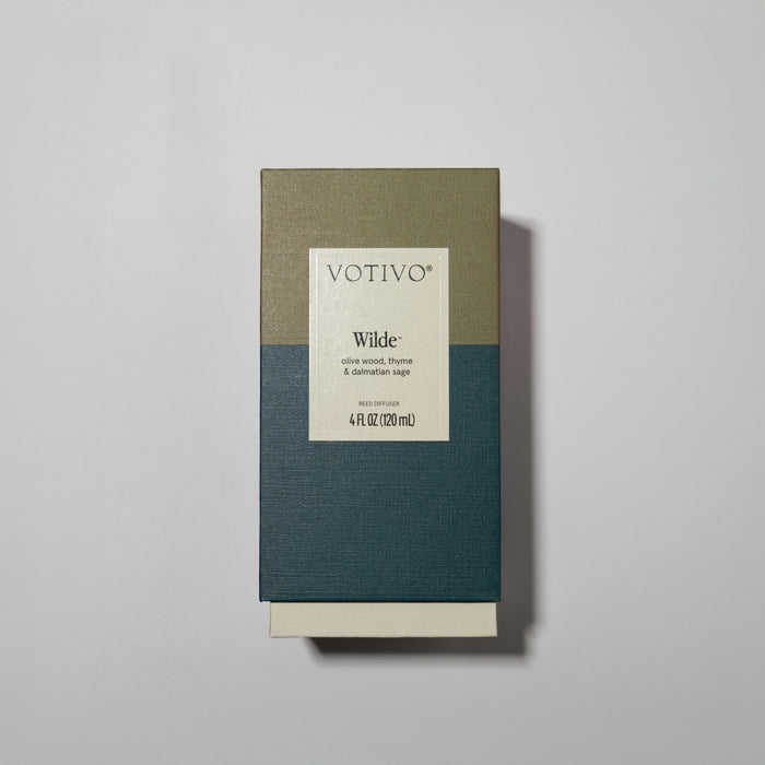 The Votivo Wilde Reed Diffuser comes in a rectangular box with olive and dark green colors and a centered label. It features elegant fiber reeds and scent notes of olive wood, thyme, and davana sage for continuous fragrance.